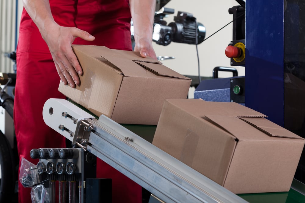 Close-up of worker putting a box on conveyor belt for shipping inside a manufacturing facility.