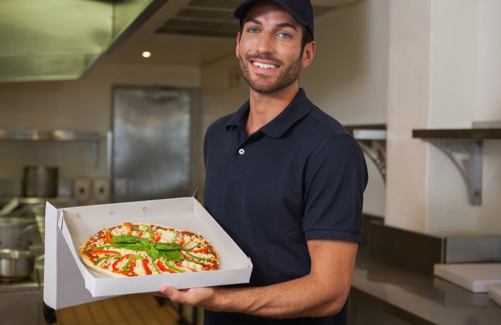 franchise pizza delivery man showing fresh pizza in a commercial kitchen