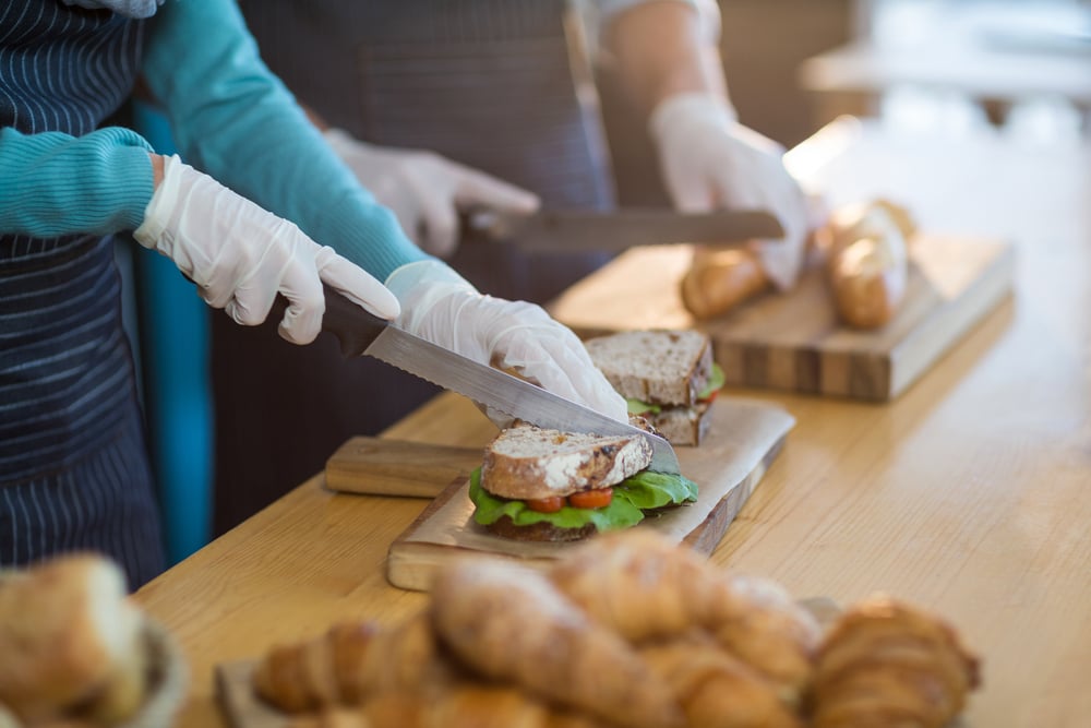 franchise worker chopping bread roll and sandwich on chopping board