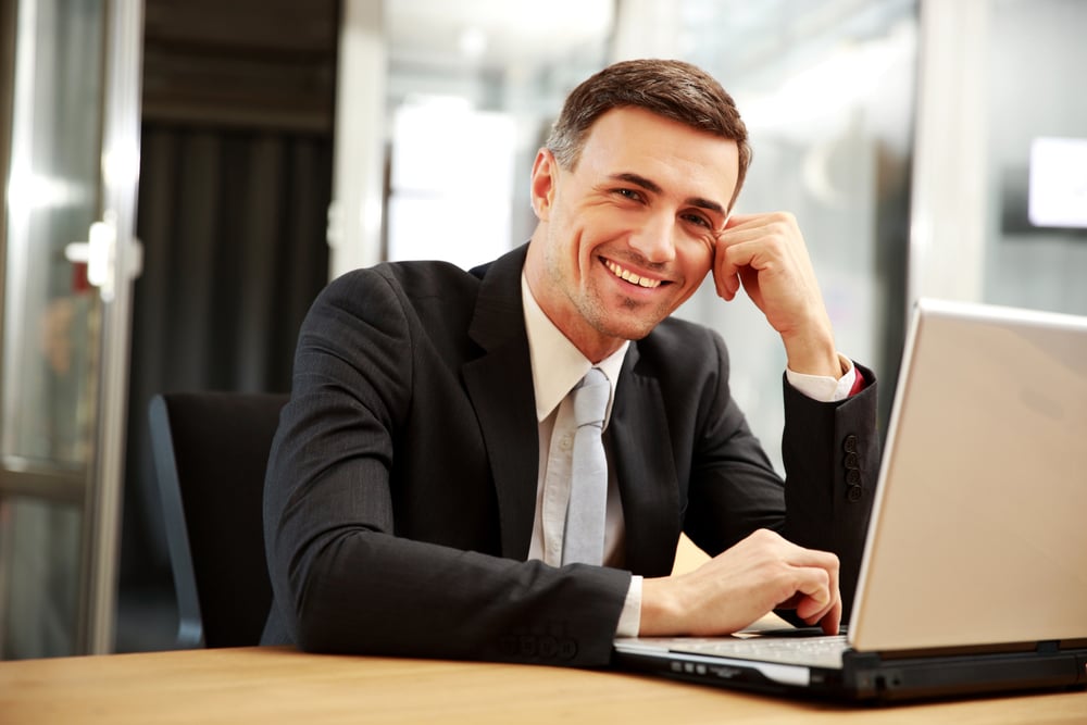 smiling male business owner at desk with laptop computer