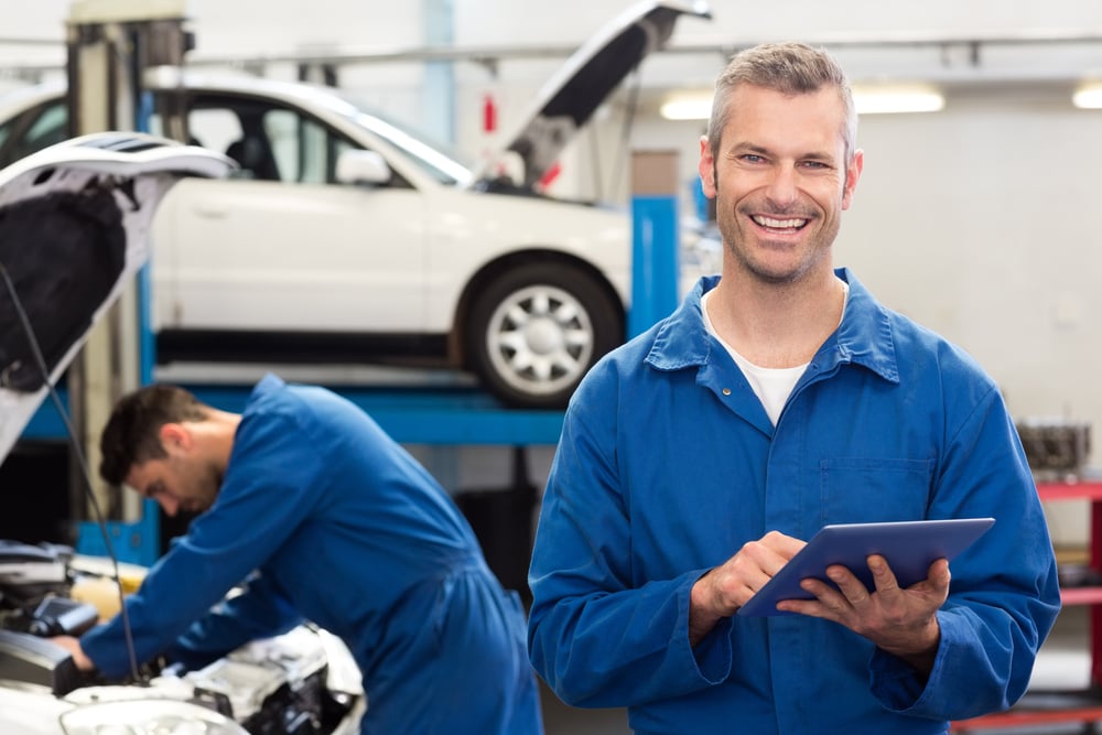 smiling auto repair business owner using a tablet at the repair garage, franchise financing