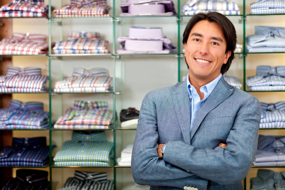 smiling male clothing store owner in front of shirt display wall